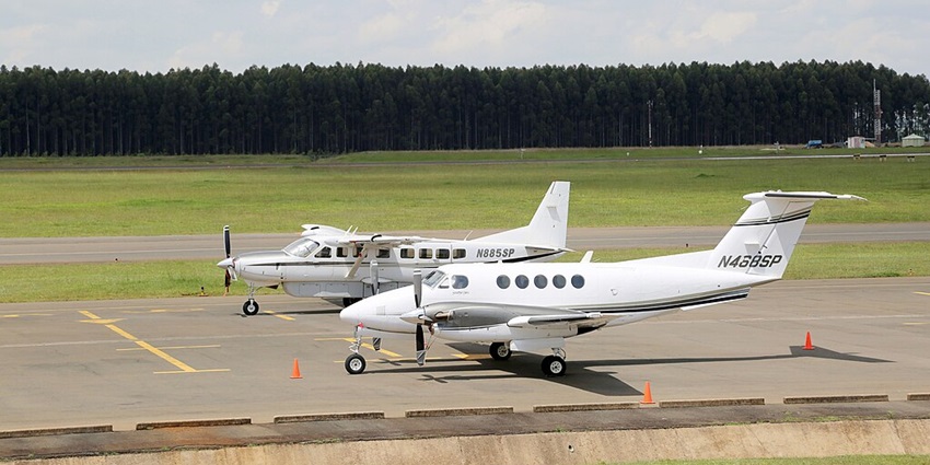 Two planes on the runway of the Eldoret International airport surrounded by grass and trees