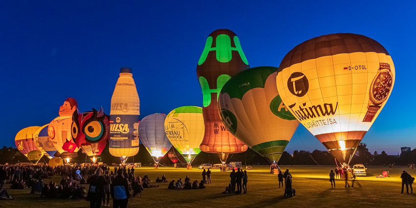 Different hot air balloons lined up with people sitting on the ground, a spot for Valentine's Day in Germany.