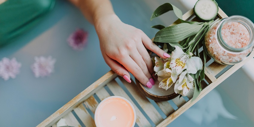 A hand with painted nails taking the cream next to flowers and candles on a tray