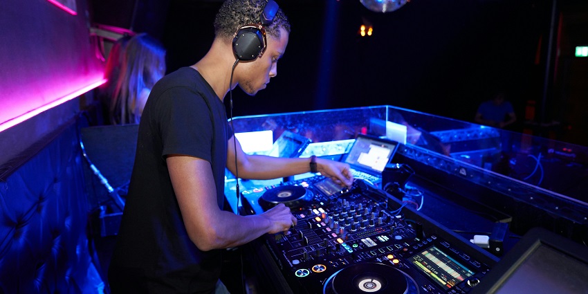 DJ wearing a black t-shirt playing music in a club and a disco ball, displaying Mauritius nightlife.