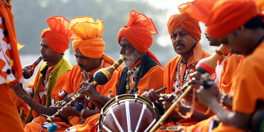 Men in orange costumes and turbans are playing different types of musical instruments.