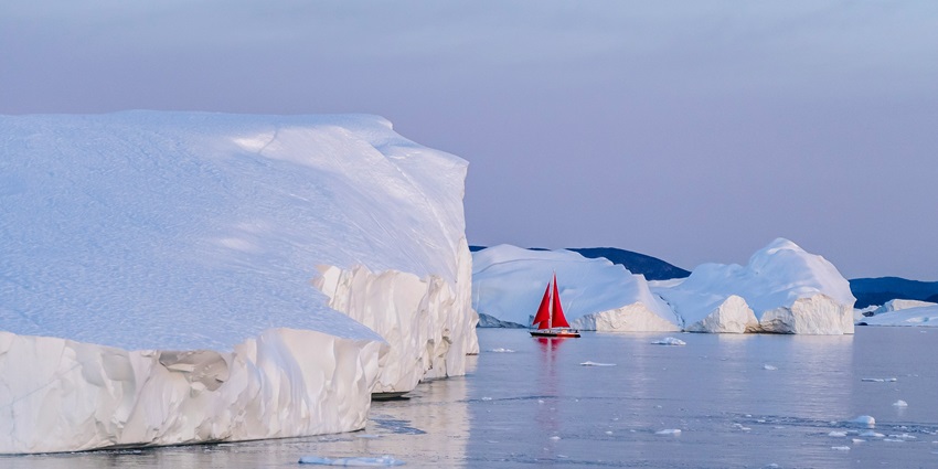 A boat with red sails is passing through Disko Bay surrounded by fjords occasionally.