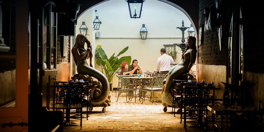 An image of a lively outdoor restaurant in New Orleans' French Quarter with diners and lights.