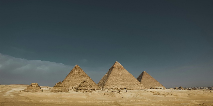 A panoramic view of the pyramids of Giza under a dark and cloudy sky is looking surreal