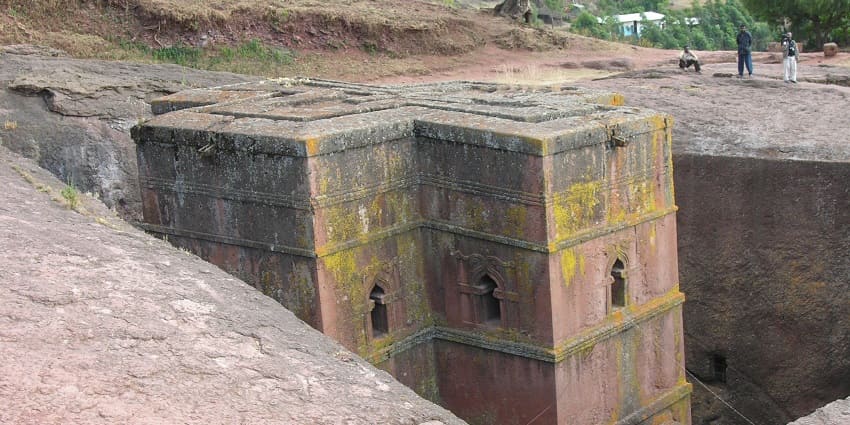 A man in a white robe is sitting inside the facade of Bet Abba Libanos Rock-Hewn Church.