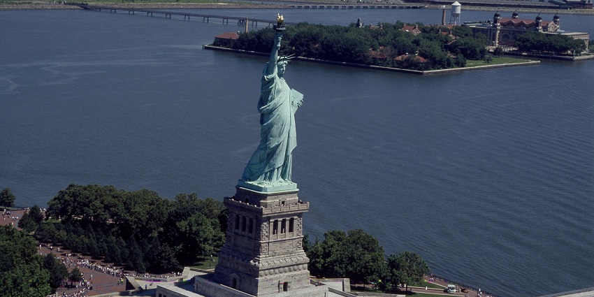 Statue of Liberty with a tall statue, people visiting and Ellis Island, one of the best things to see in New York.