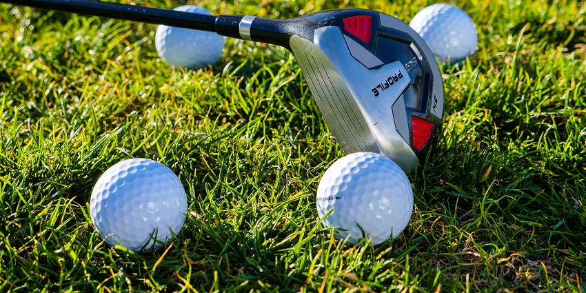 An close-up of a golf club with multiple golf balls on lush grass