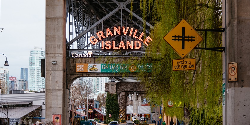 A Granville Island signboard on a street and showing direction against an urban background.