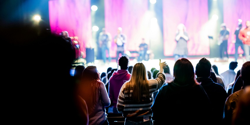 Crowded street scene at a music festival with people enjoying live music on a stage.