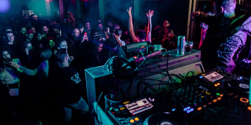 People inside a nightclub with an artist performing, people dancing under neon lights.