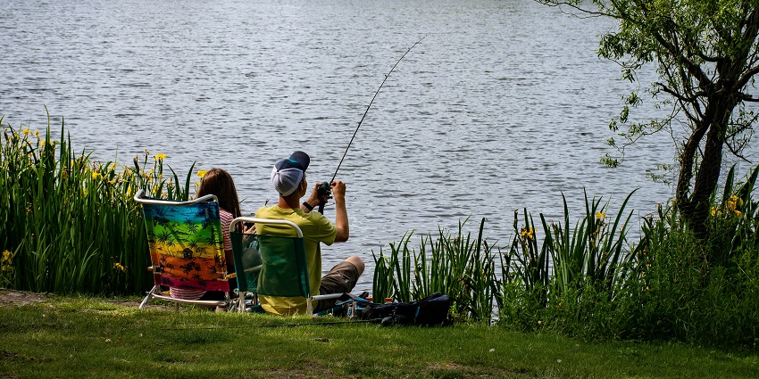 An image of the calm river with a person fishing and holding a fishing rod.