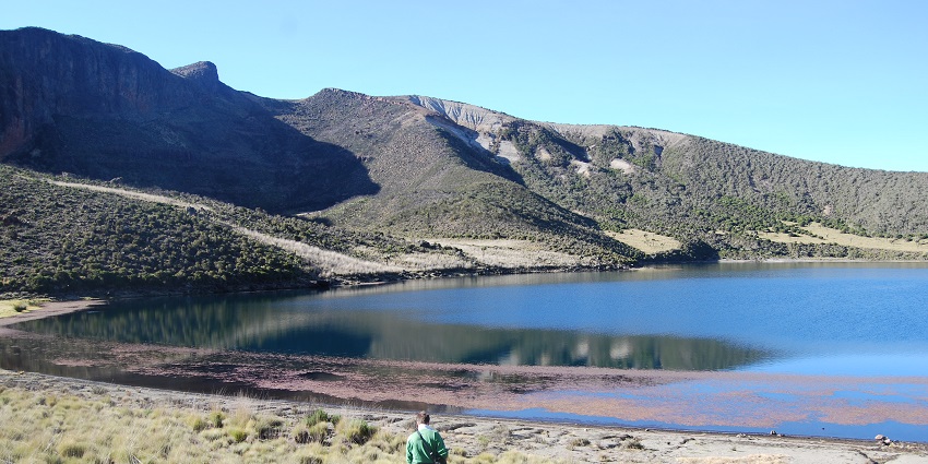 A man standing with a dog in the dry grassland near the mount kenya lake with hills.