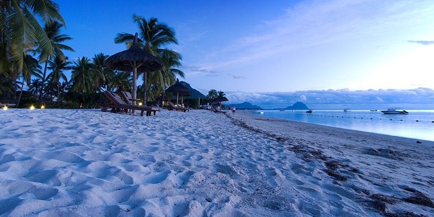 Flic-en-Flac beach during the blue hour with empty beach chairs, palm trees and dim lights.