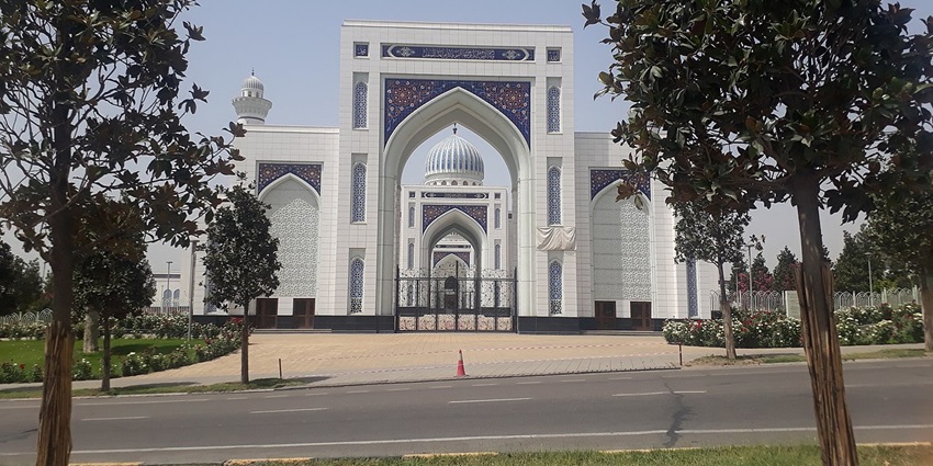 Mosque with its multiple white and green minarets and stairs surrounded by tall trees.