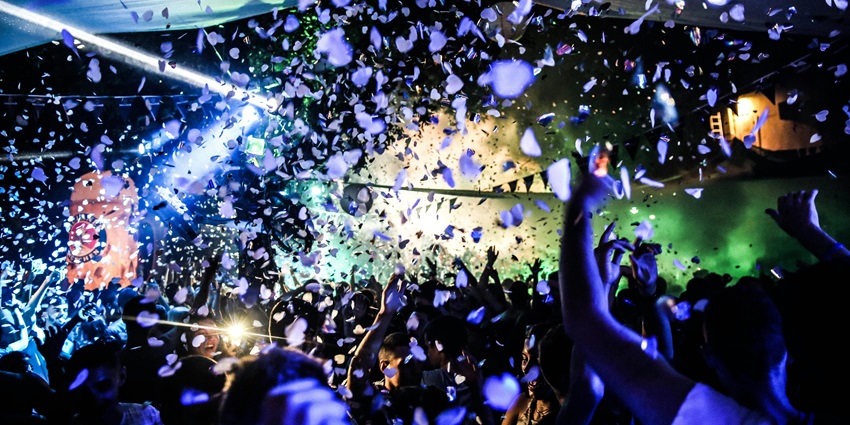 An image of a crowd of people dancing energetically at a rave party inside a nightclub