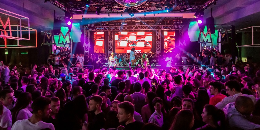 Crowd of people dancing inside a nightclub with vibrant pink lights and a DJ performing