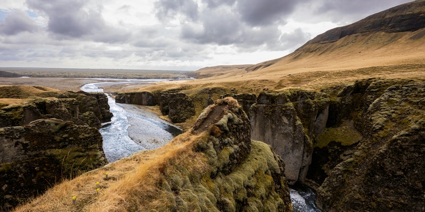 An Image of a river flowing amongst the rocky terrain, under a cloudy sky.