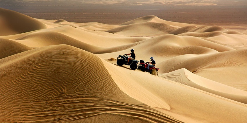 Tourists are riding on quad bikes on the sand dunes of a desert to enjoy adventure safari.