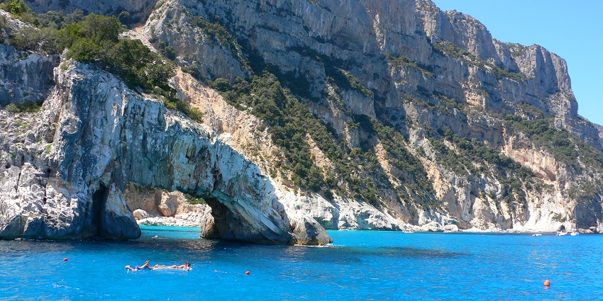 Coastal area with turquoise waters and rugged cliffs, highlighted in Sardinia travel guide.