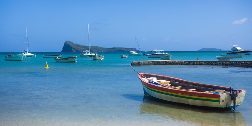 Boats and yachts are resting in the clear blue water by the seashore of Grand Baie.