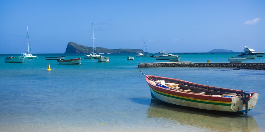 Grand Baie with bright blue sea, multiple boats on the sea and cars parked near the trees.