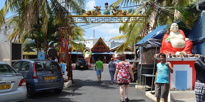 Grand Baie entrance with the people entering the bazaar and cars parked on the sides.