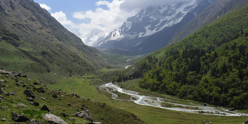 A majestic view of a lush green valley in Uttarakhand surrounded by mountains all around