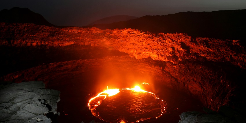 A lava lake inside the pit of the Erta Ale Volcano is burning and erupting smoke.