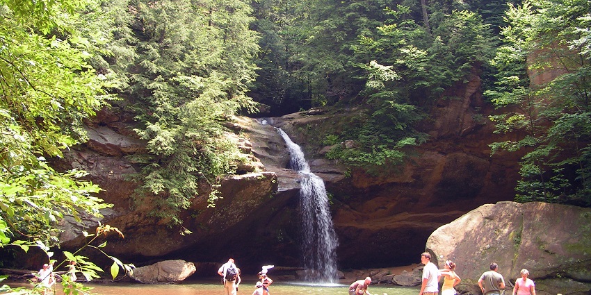 Hocking Hills State Park with a waterfall flowing down and people enjoying the waters