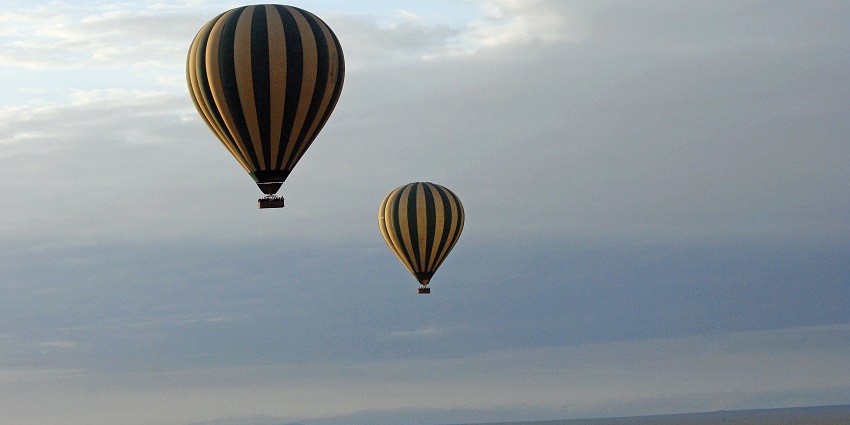 Two hot air balloon safaris in the air floating over the Serengeti National Park landscape.