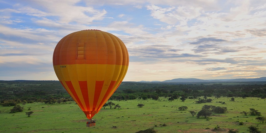 Hot air balloon floating in Masai Mara National Reserve with greenery and mountains.