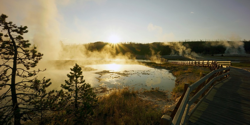 A boardwalk made up of woods beside the hot springs with sunset in the background.