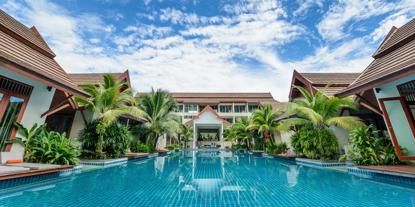 A picture of a luxurious hotel resort with a really big swimming pool amidst tall palm trees.