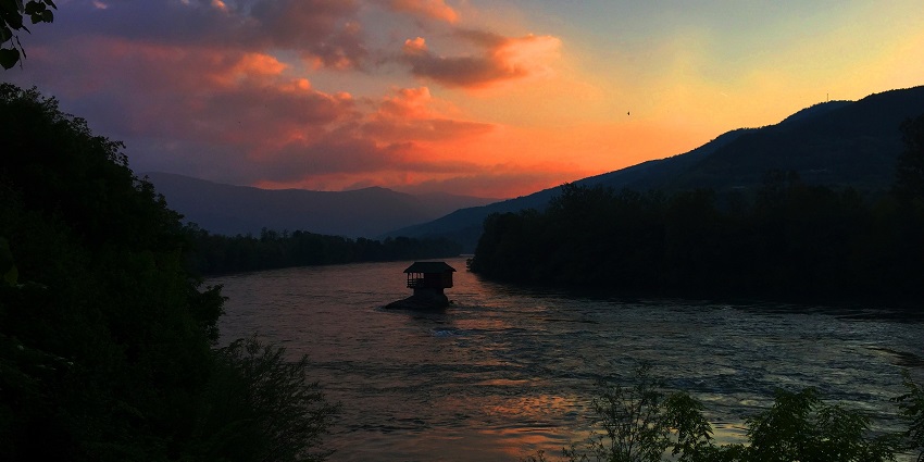 A view of the House on the Drina, a charming cabin-like home perched on a river stone.