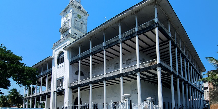 House of wonders with white architecture, multiple floors, cars parked and a clock tower