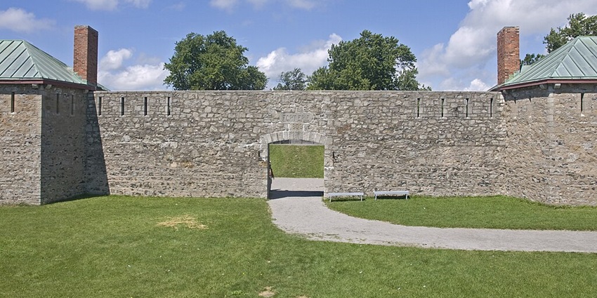 A view of the stone wall at Old Fort Erie with green grass, trees, and a cloudy sky in the background.