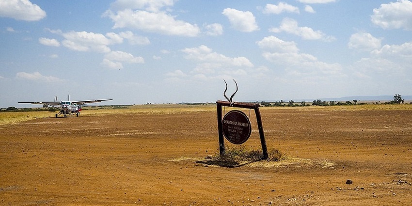 Masai Mara airstrip in a sandy land, a sign board and an aeroplane far behind it