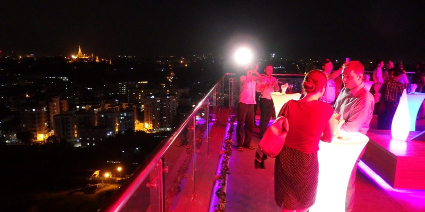 A rooftop bar with bright pink lighting and glass railing and the people enjoying