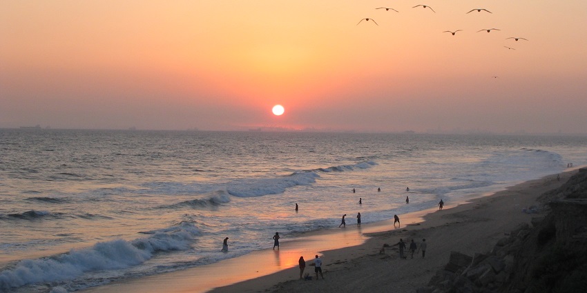 High waves are crashing on Huntington Beach, with a few people on the shore during sunset