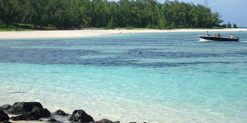 A boat in the sea is approaching the shore of Île aux Cerfs carrying a few passengers.
