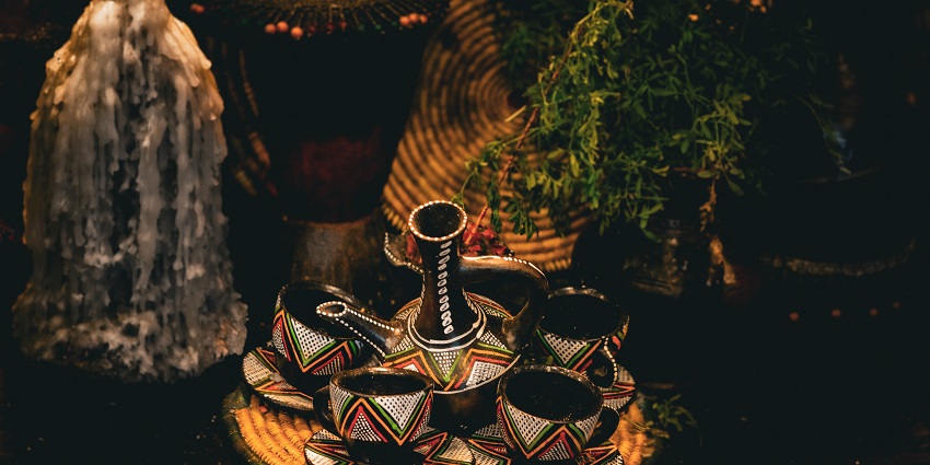 Colourful coffee cups and a coffee pot have been placed on a table near a melted candle.