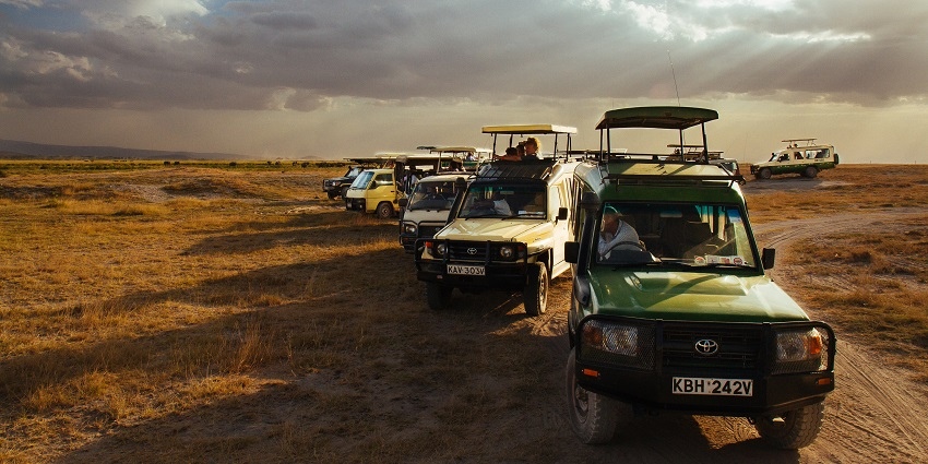 Several vehicles with people on a game drive in Amboseli National Park during sunset.