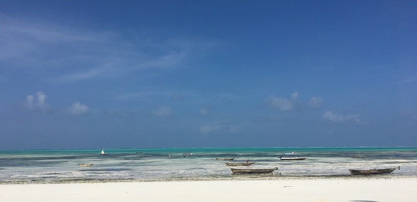 A crystal clear water surrounding the Jambiani Beach, which has several small boats on it.