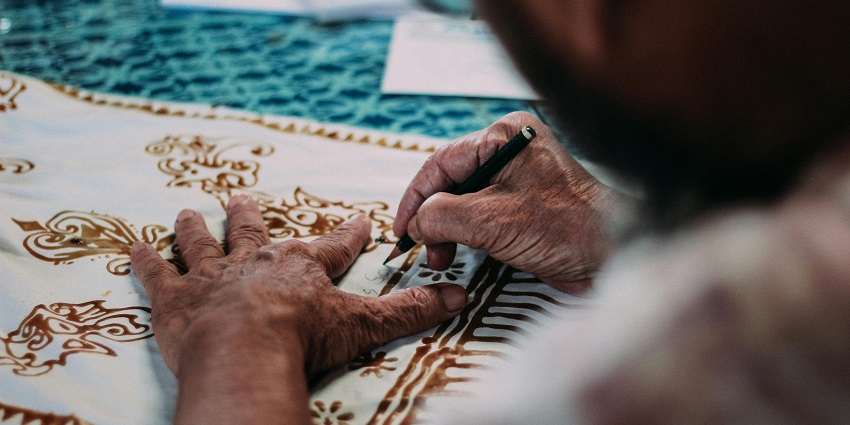 Image of a man crafting a cloth with beautiful designs in brown colour