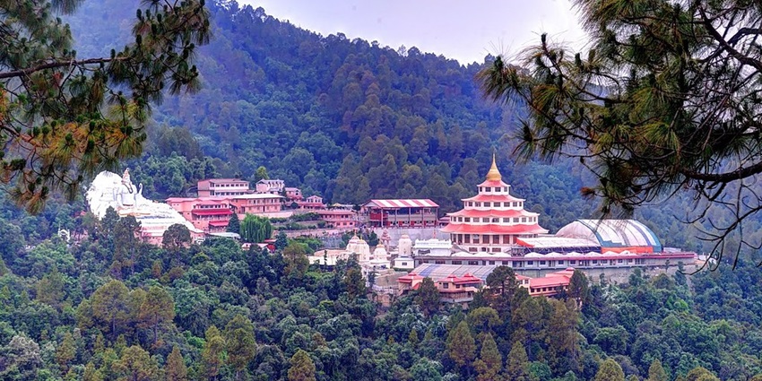 Image of an ashram and the temple surrounded by lush green hills under clear blue sky