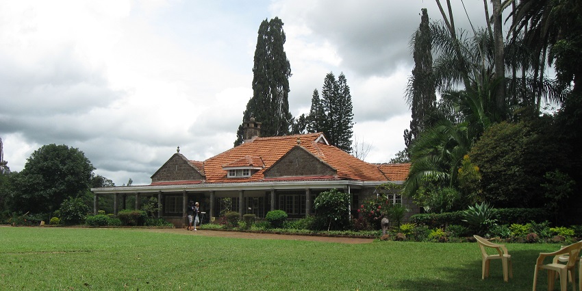 Chairs lying on the lawn of Karen Blixen Museum with its building surrounded by greenery.