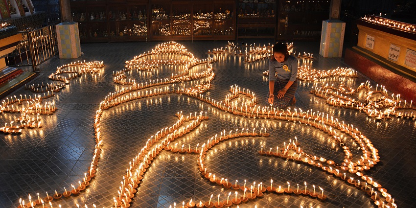 Image of a lady in a temple lit up the candles in design - during Kason Full Moon festival