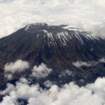 Mount Kilimanjaro with some snow on the top and mountain all surrounded by clouds