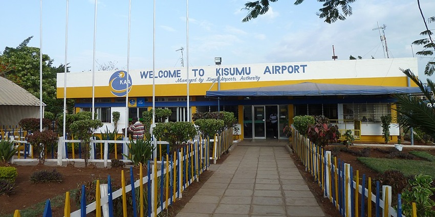 Kisumu airport entrance showing airport name, wing of a plane, utility vehicles and a man
