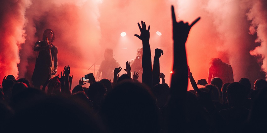 People raising their hands in the air while a band performs in the background with smoke